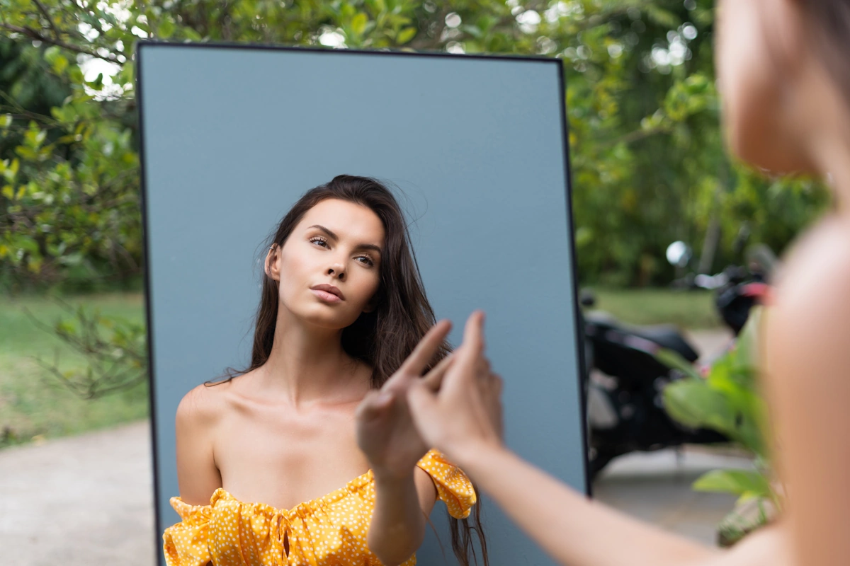 Une femme en robe jaune qui se regarde dans un mirroir