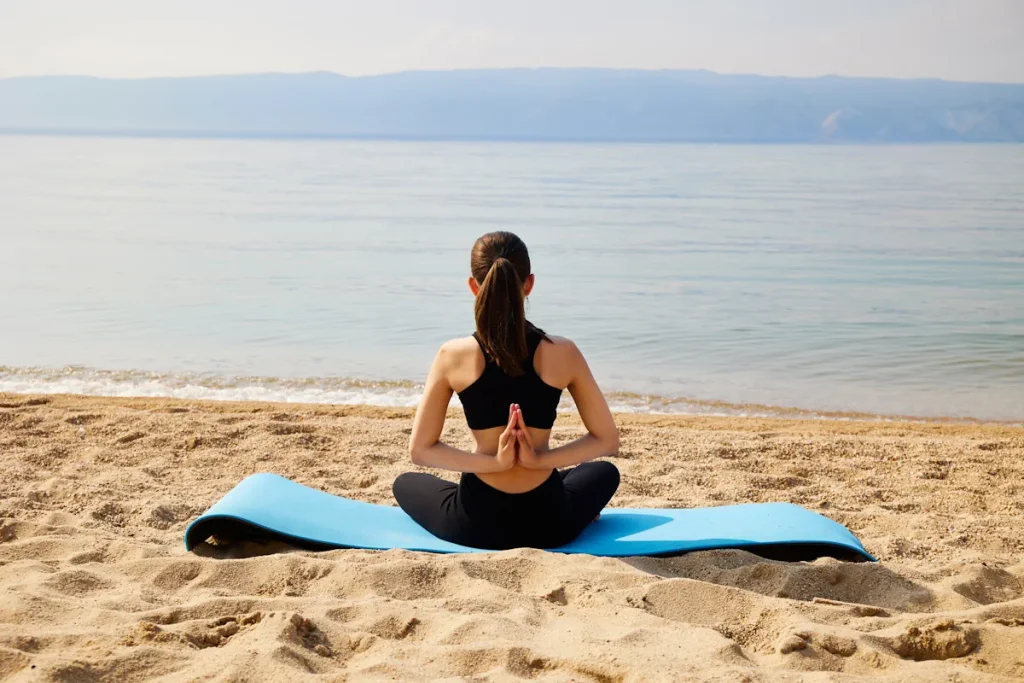 Une femme sur un tapis de yoga qui médite sur la plage face à la mer