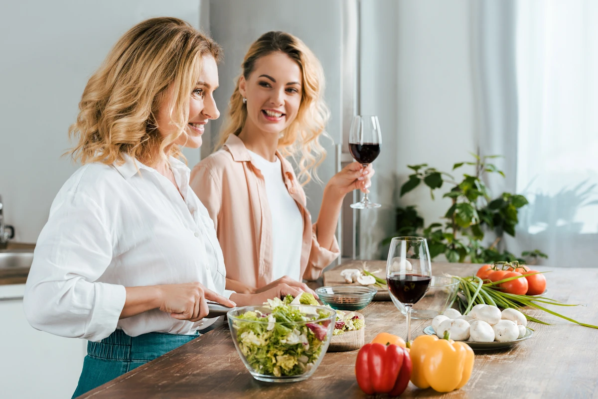 Une maman et sa fille entrain de cuisiner un verre de vin à la main