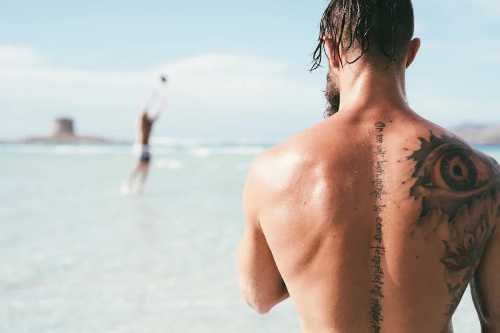 Un jeune homme à la plage face à la mer avec un tatouage dans le dos