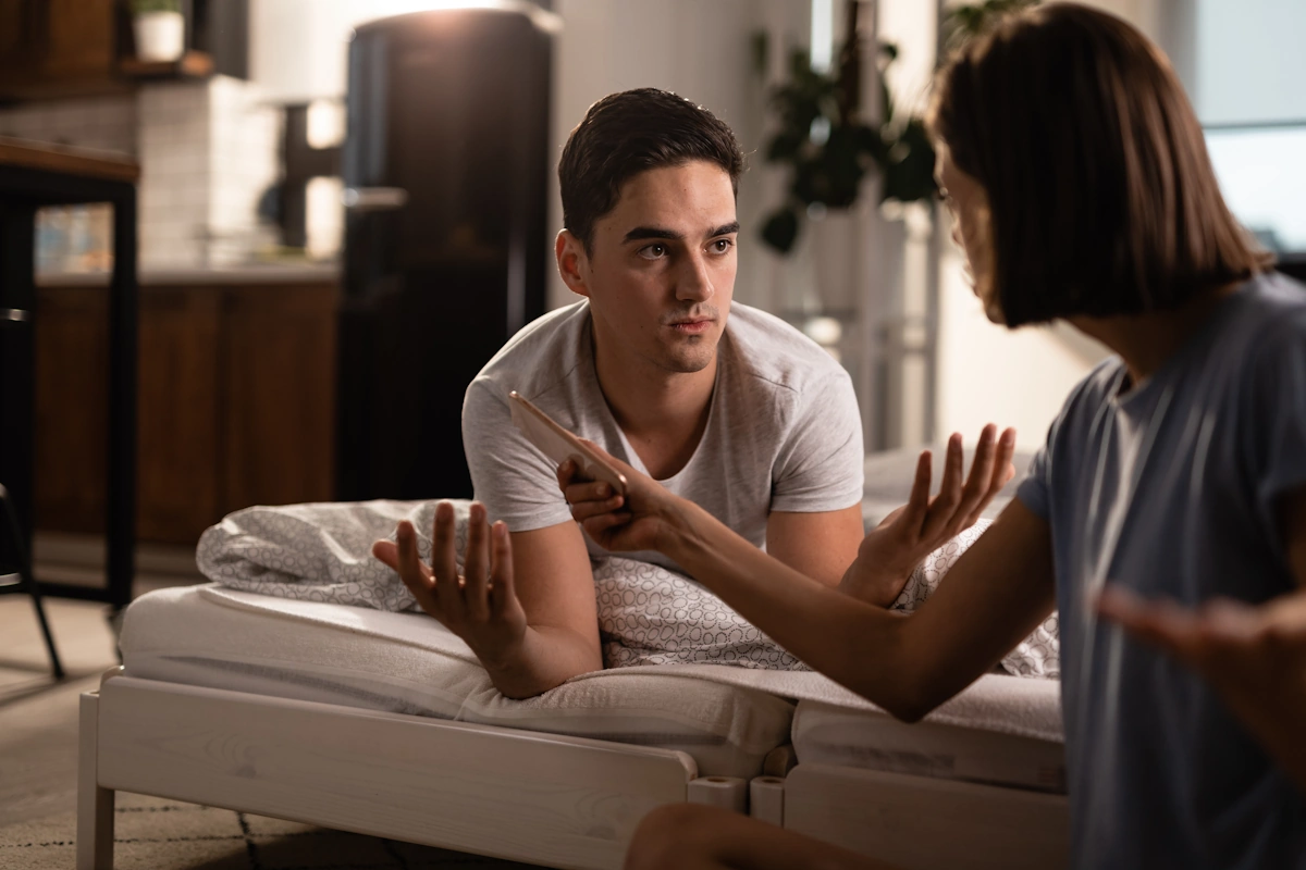 Un homme sur le canapé qui discute avec sa femme qui tient un téléphone