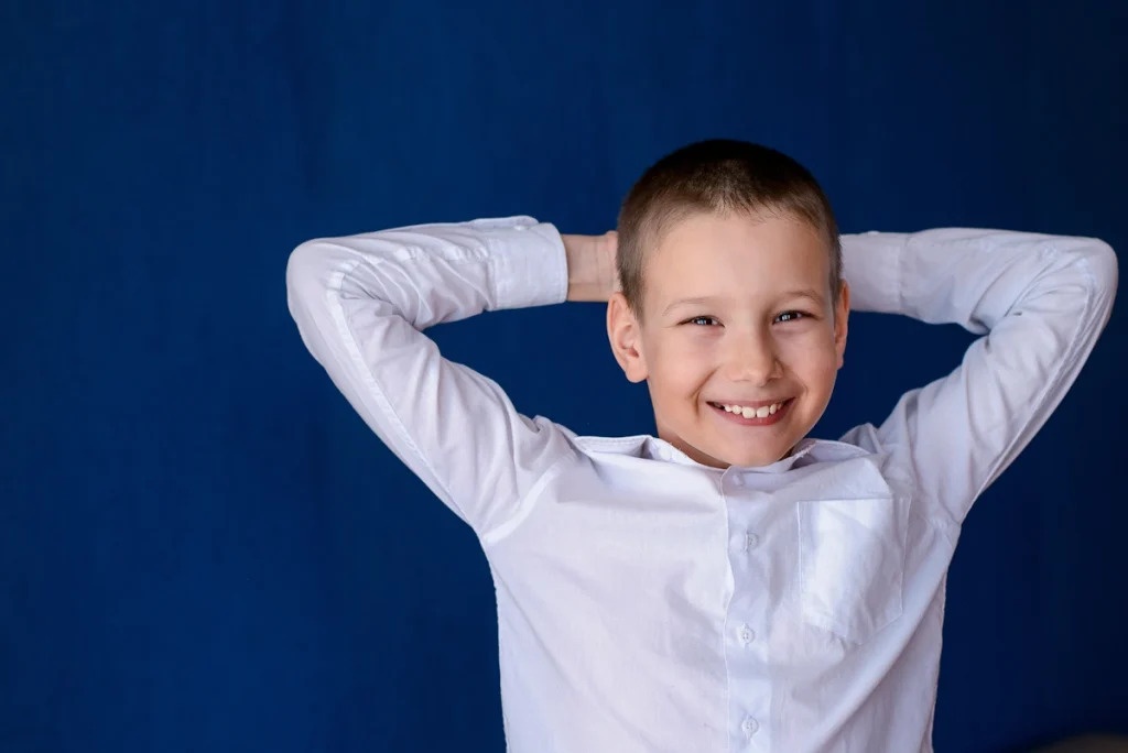 Un petit garçon avec une chemise blanche allongée sur le dos avec le sourire