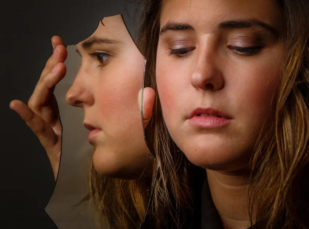 Une femme qui tient un miroir cassé dans lequel on voit son reflet