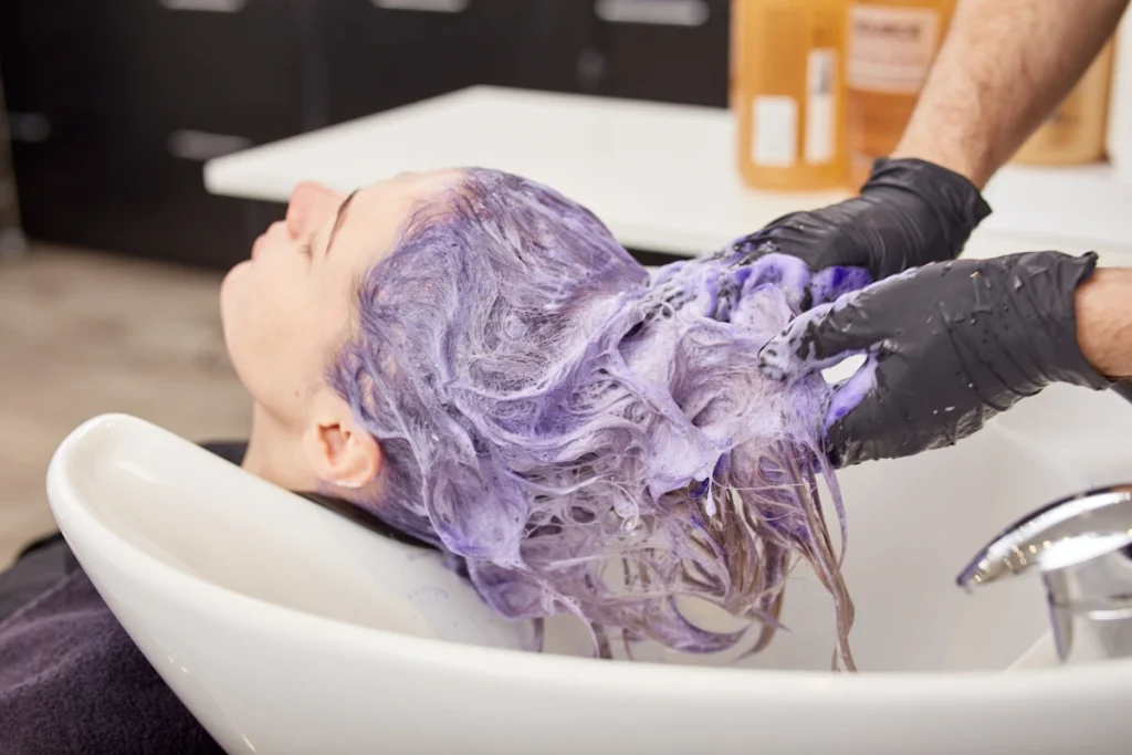 Une femme avec les cheveux violets qui est sur le bac d'une coiffure