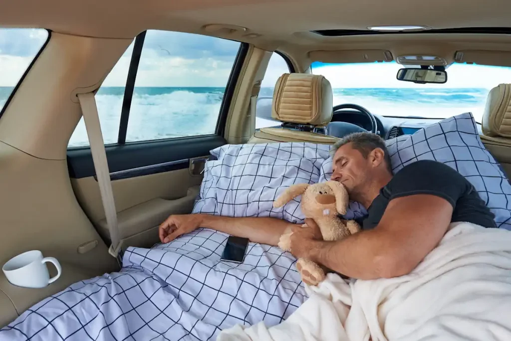 Un homme qui dort dans sa voiture avec une peluche