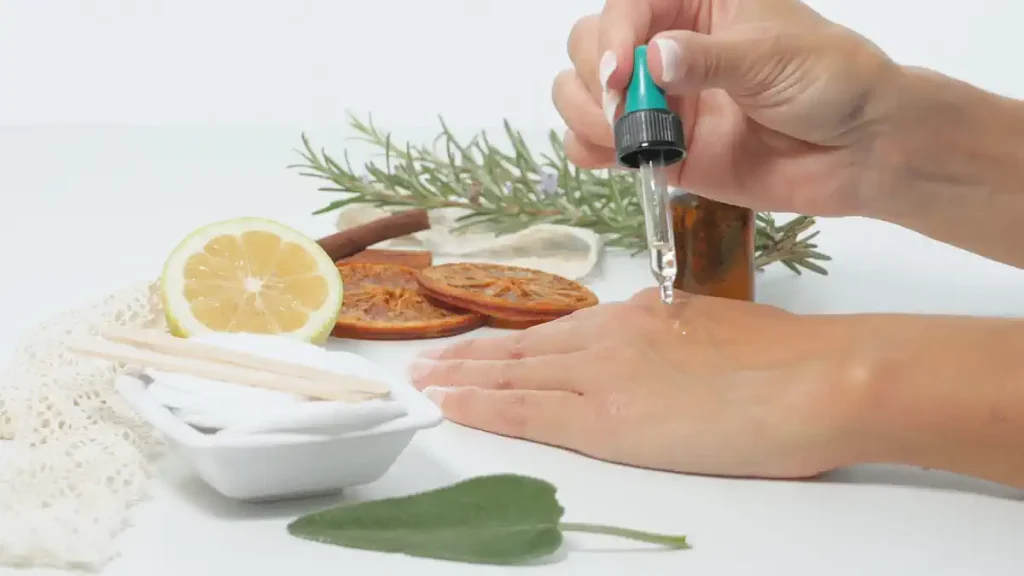 Une personne qui verse de l'huile essentielle avec une pipette sur la peau de sa main posée à côté d'un citron et de thym