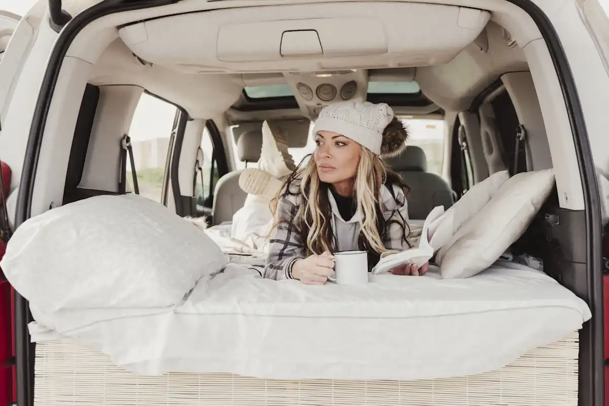Une femme qui se détend dans sa voiture aménagée avec des coussins