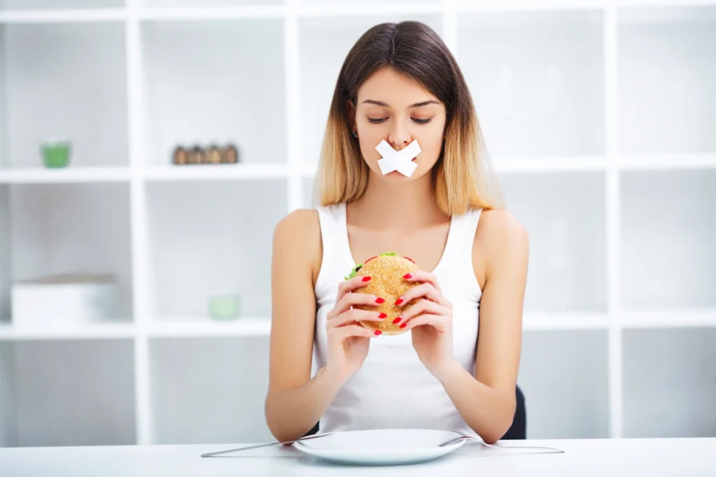 Une femme avec du scotch sur la bouche et qui tient un hamburger dans ses mains
