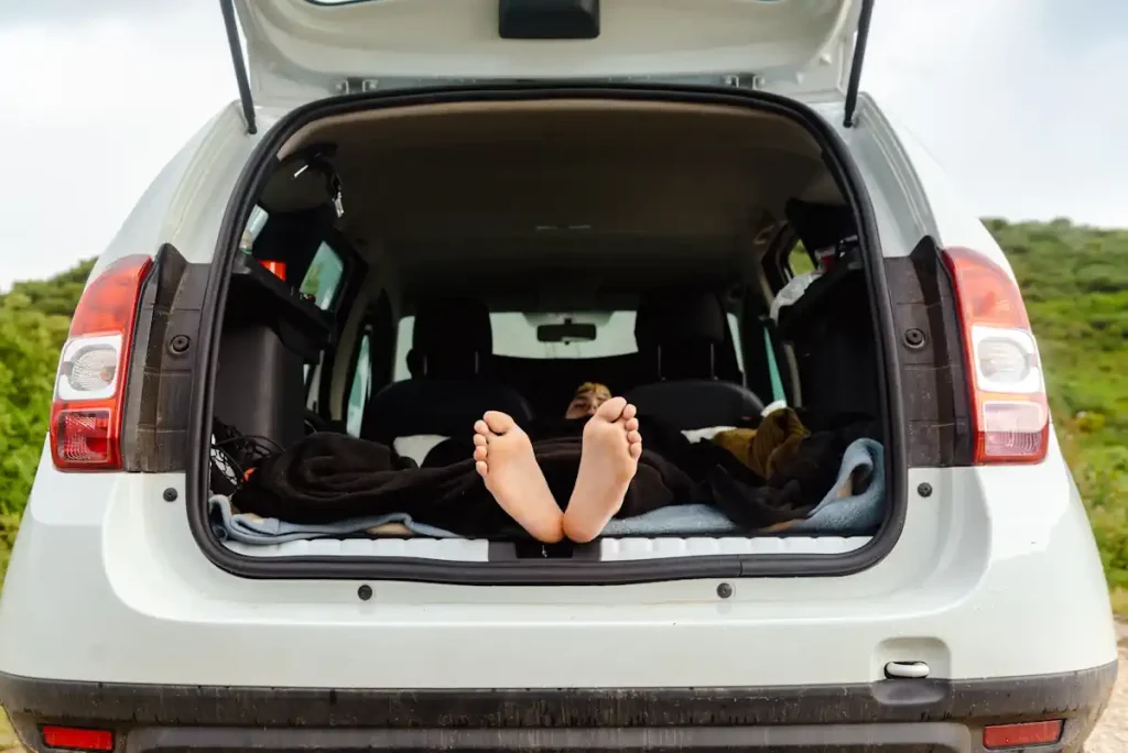 Une personne qui dort dans sa voiture avec les pieds qui dépasse