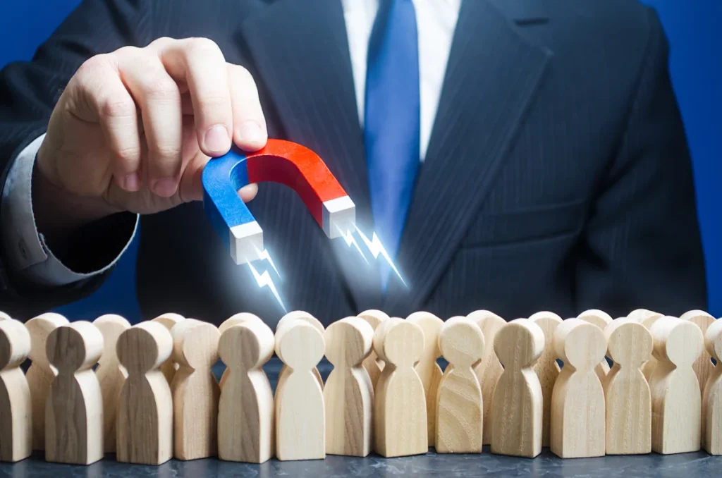Un homme en costard qui tient un aimant pour attirer des petits personnages en bois posés sur une table
