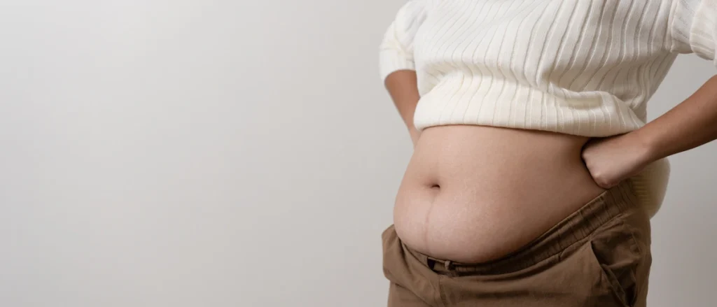 Une femme en haut blanc et pantalon marron qui montre son ventre