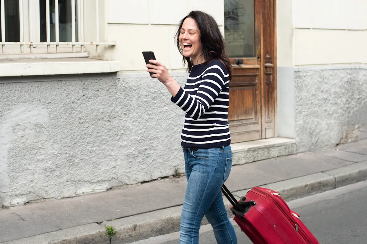 Une femme qui tire sa valise en marchant et en regardant son smartphone
