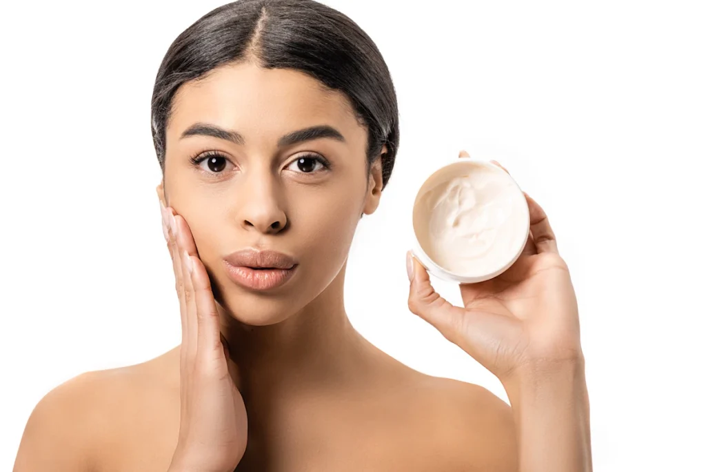 Une femme qui applique une crème sur son visage en tenant le pot dans l'autre main