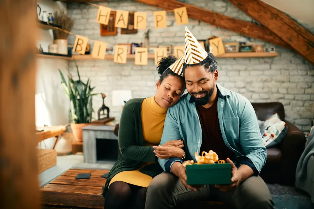 Un homme et une femme assis en tenant un cadeau avec le mot joyeux anniversaire en arrière