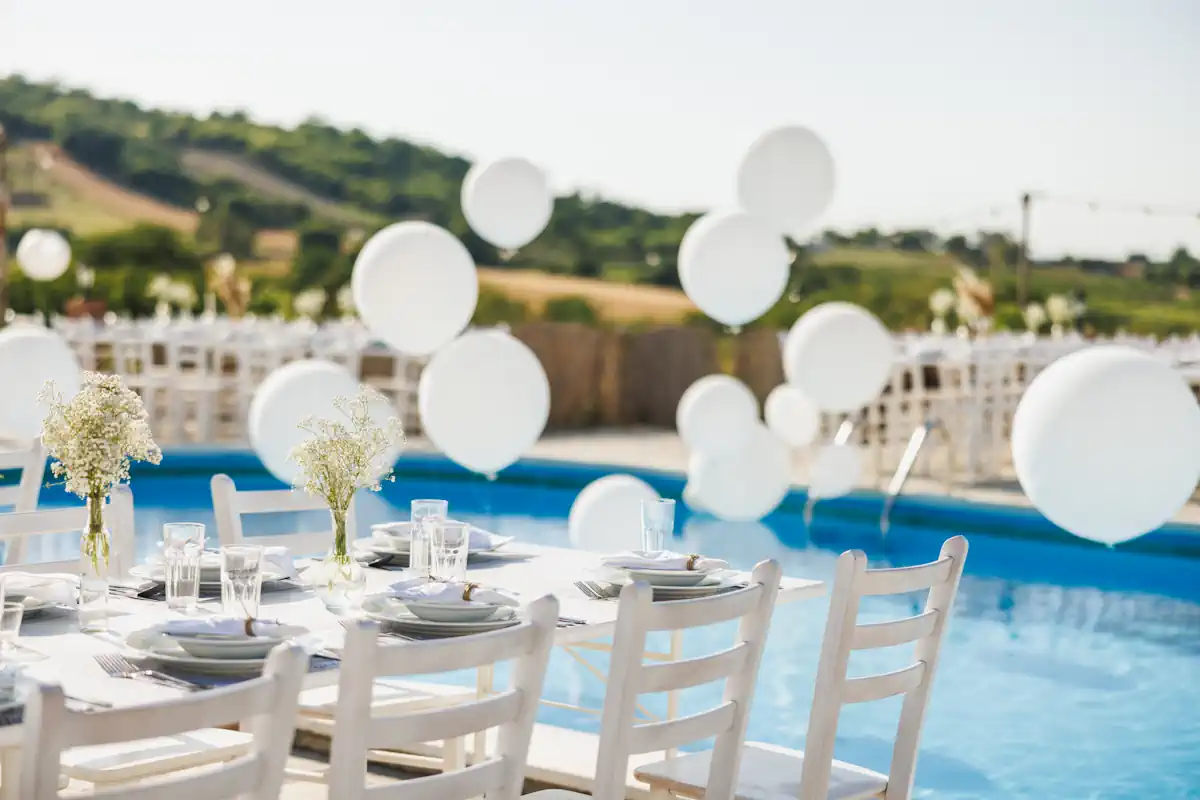 Un espace décoré avec des ballons blanc, des chaises blanches et des fleurs