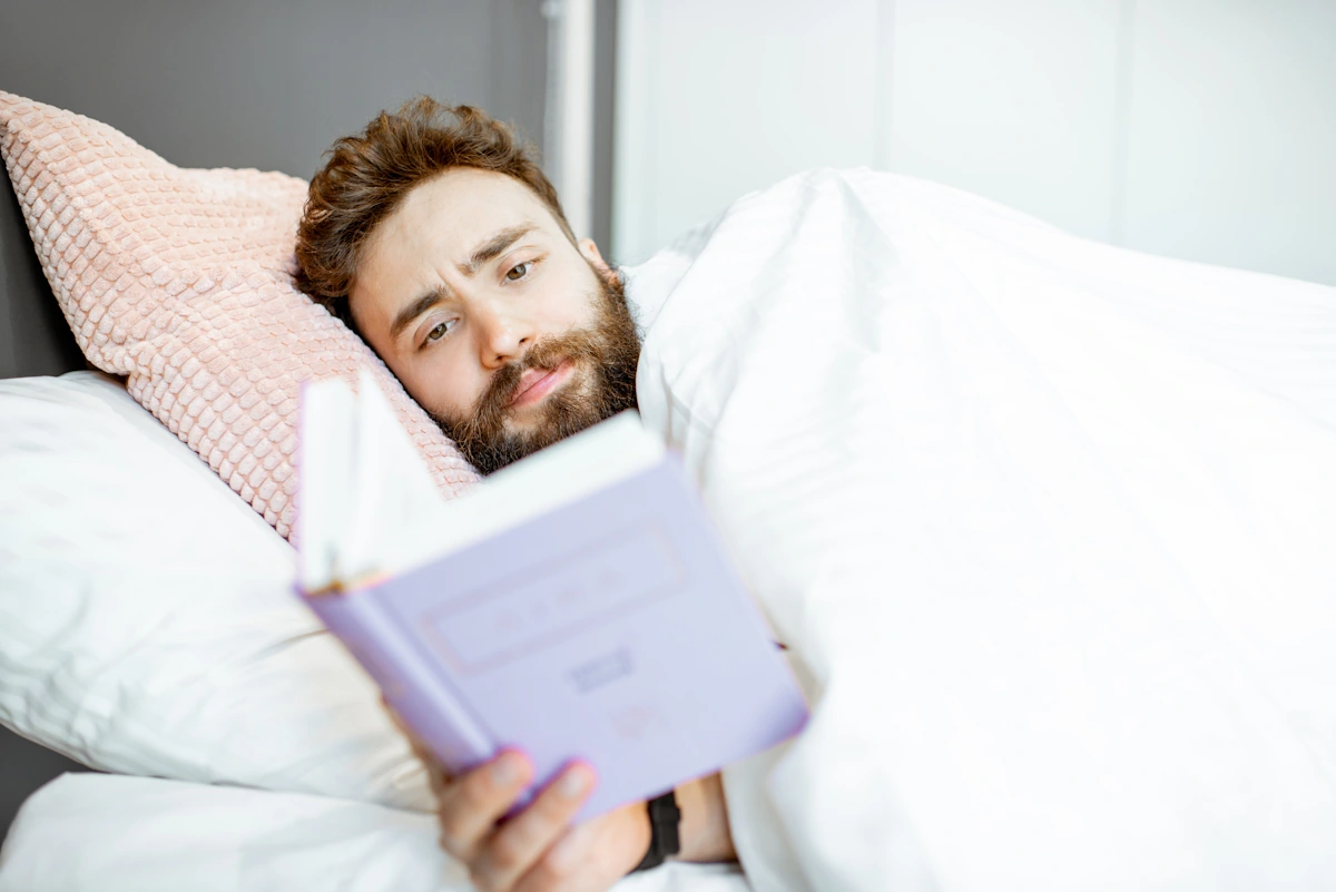 Un homme dans son lit entrain de tenir un livre dans sa main