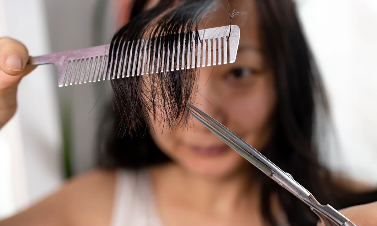 Une femme qui se coupe les cheveux avec un ciseau et une peigne