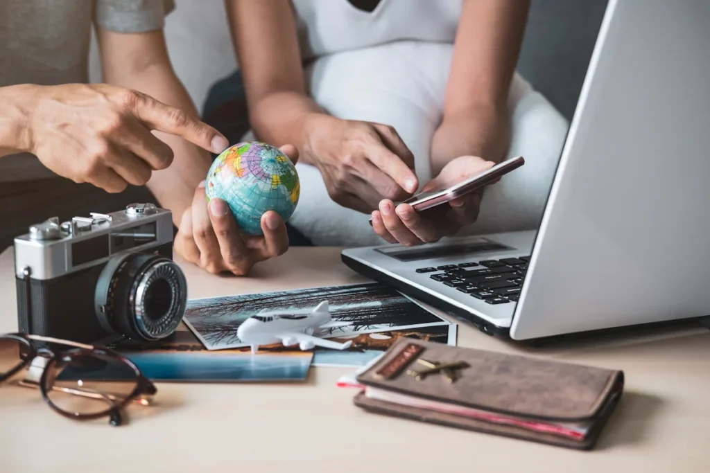 deux personnes qui regarde une mini globe terrestre, un smartphone devant un ordinateur, un appareil photo et des documents sur une table