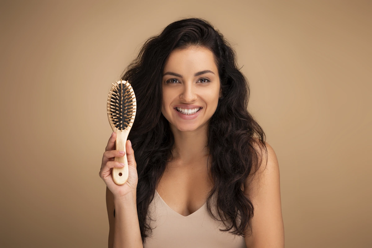 Une femme avec les cheveux longs et épais qui tien tune brosse en bois dans la main