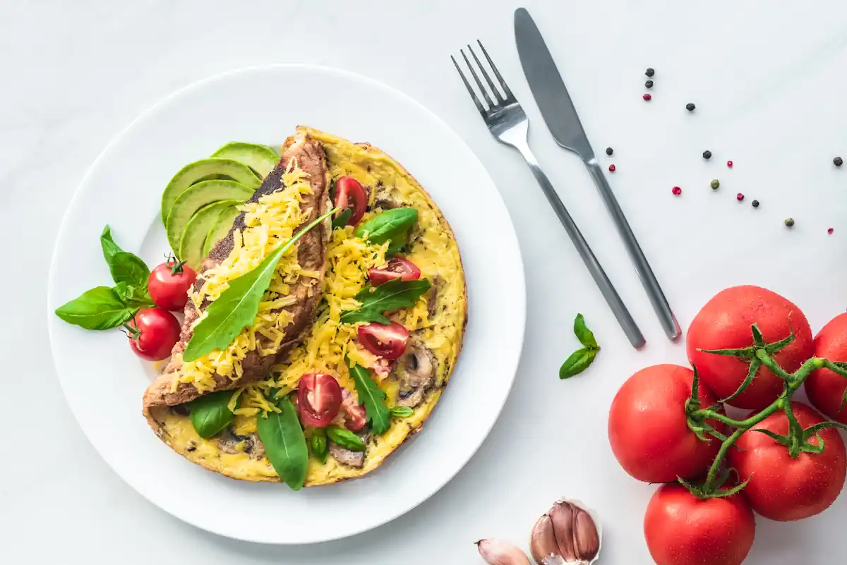 Une assiette d'omelette avec des herbes à côté d'une fourchette et d'un couteau ainsi que quelques tomates