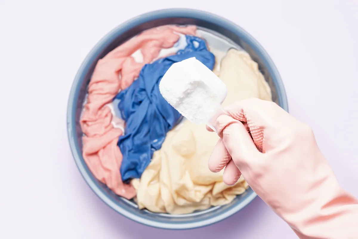 Une personne qui ajoute de la poudre blanche dans un bac de linge à laver