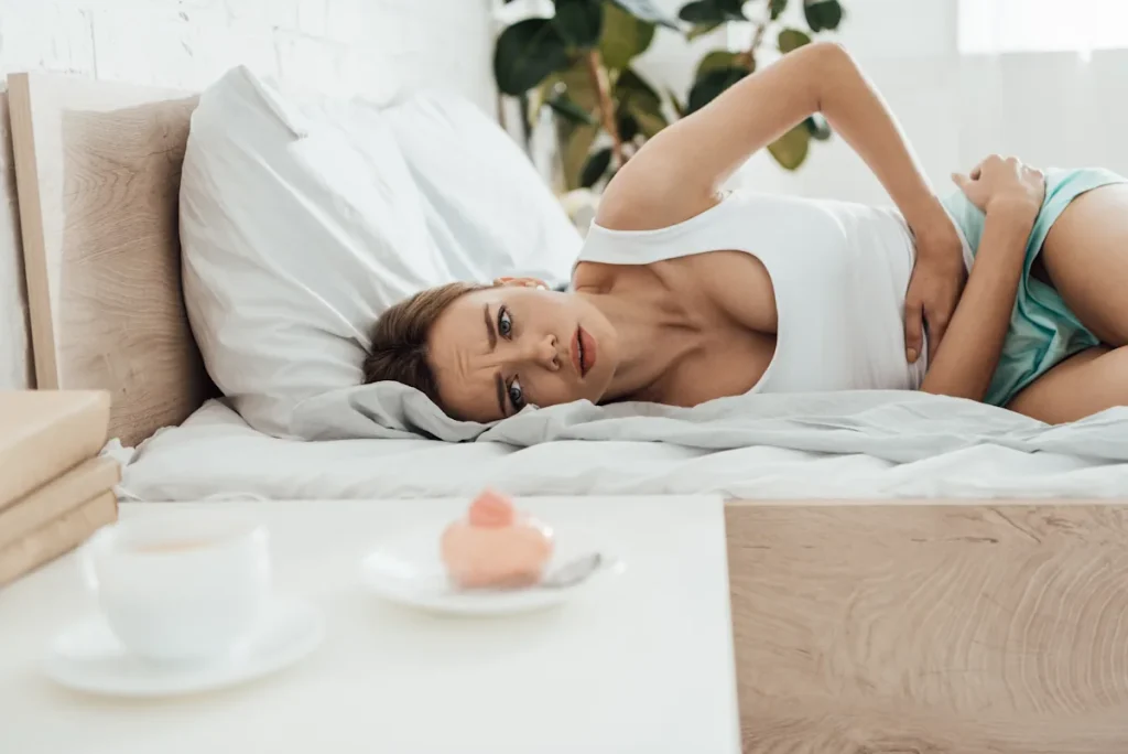 Une femme qui se tient le ventre allongée sur un lit