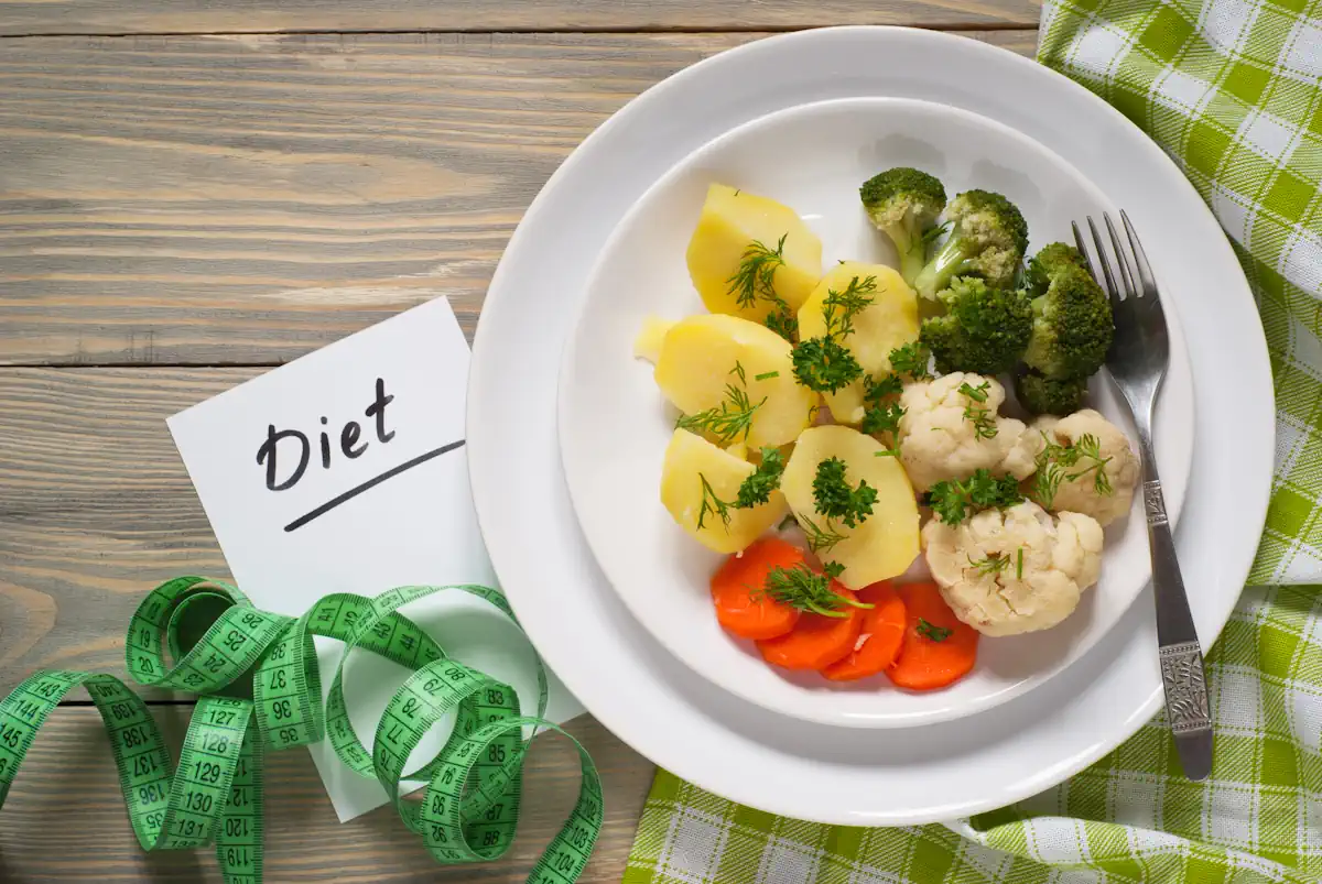 Une assiette avec du brocolis, des pommes de terres, des choux fleurs et des carottes posée à coté d'un mètre ruban vert et d'un mot Diet
