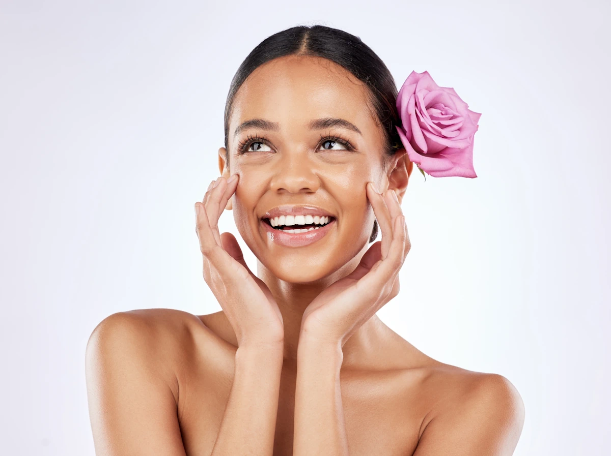 Une femme qui sourit avec une peau éclatante et une rose sur les oreilles