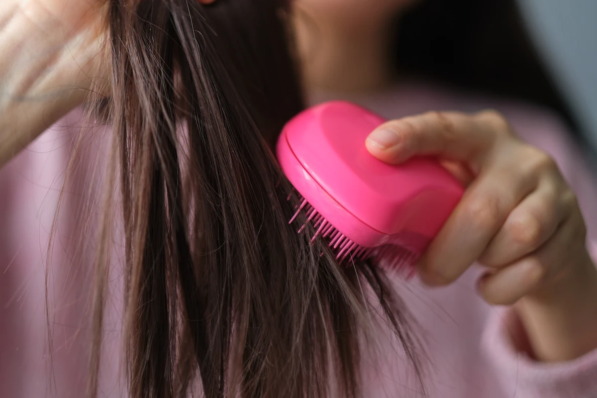 Une femme qui démêle les cheveux avec une brosse rose