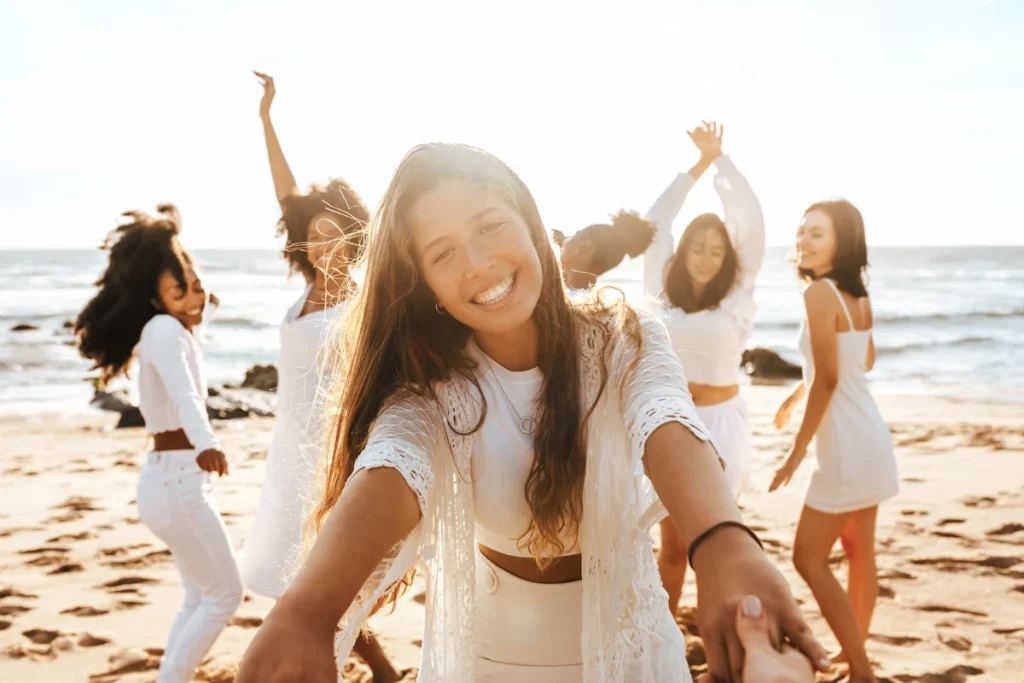 Une femme qui se met en avant face à un groupe de femme qui danse en blanc sur la plage