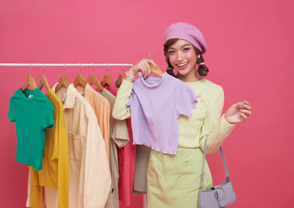 Une femme avec une tenue jaune et un bonnet violet qui regarde des vêtements sur un portant