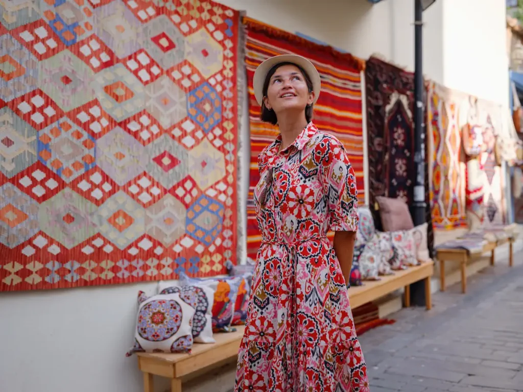 Une femme en robe dans une rue où sont présentés des tapis colorés